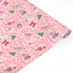 A roll of wrapping paper featuring a whimsical pattern of pink wavy lines, ballerinas, Christmas trees, presents, and nutcrackers on a light pink background.