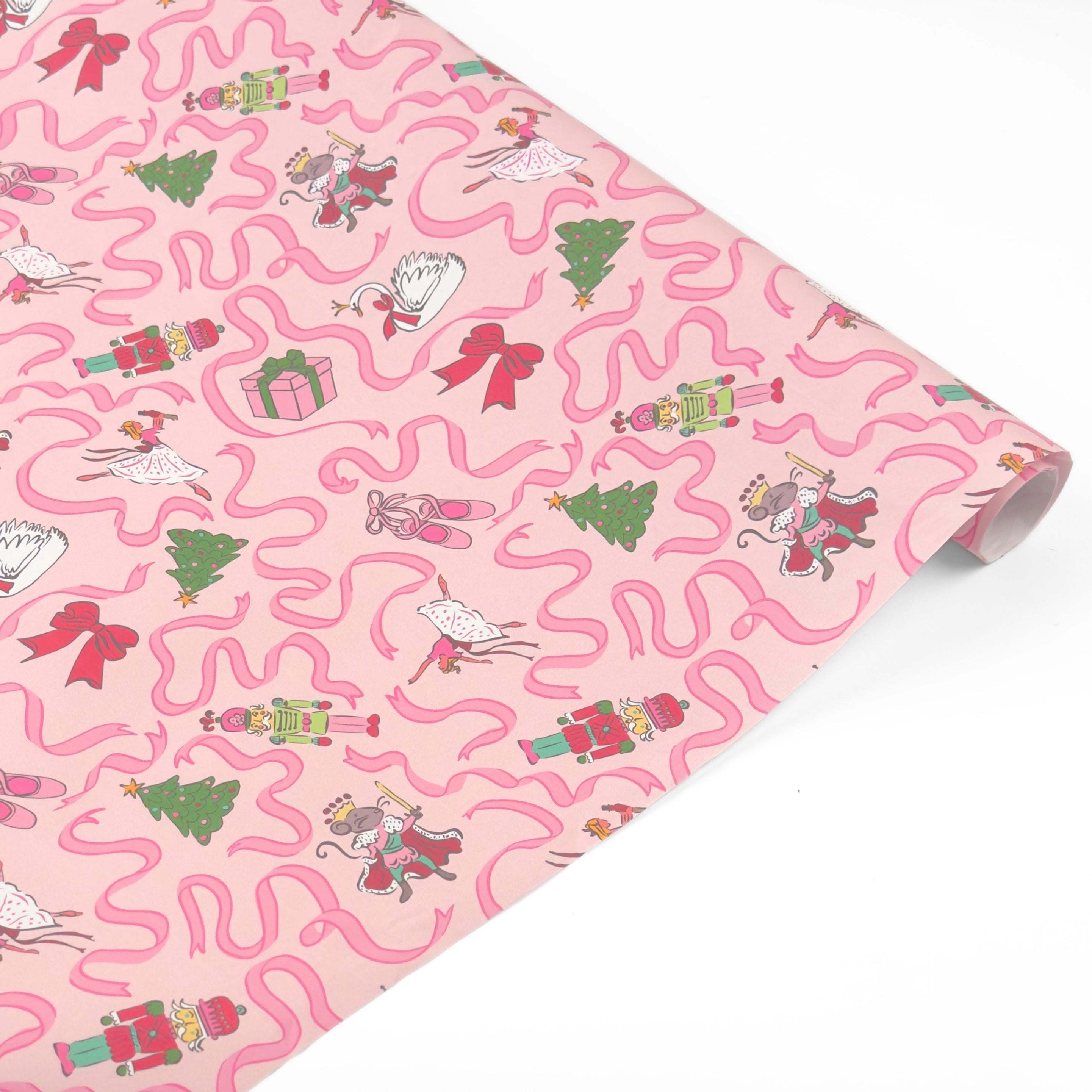 A roll of wrapping paper featuring a whimsical pattern of pink wavy lines, ballerinas, Christmas trees, presents, and nutcrackers on a light pink background.