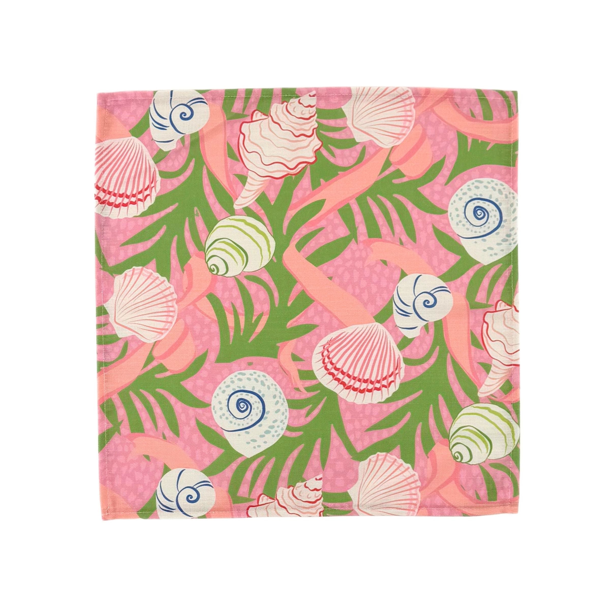 Pink cloth dinner napkins featuring colorful seashells, tropical green foliage, and playful coastal inspired patterns.