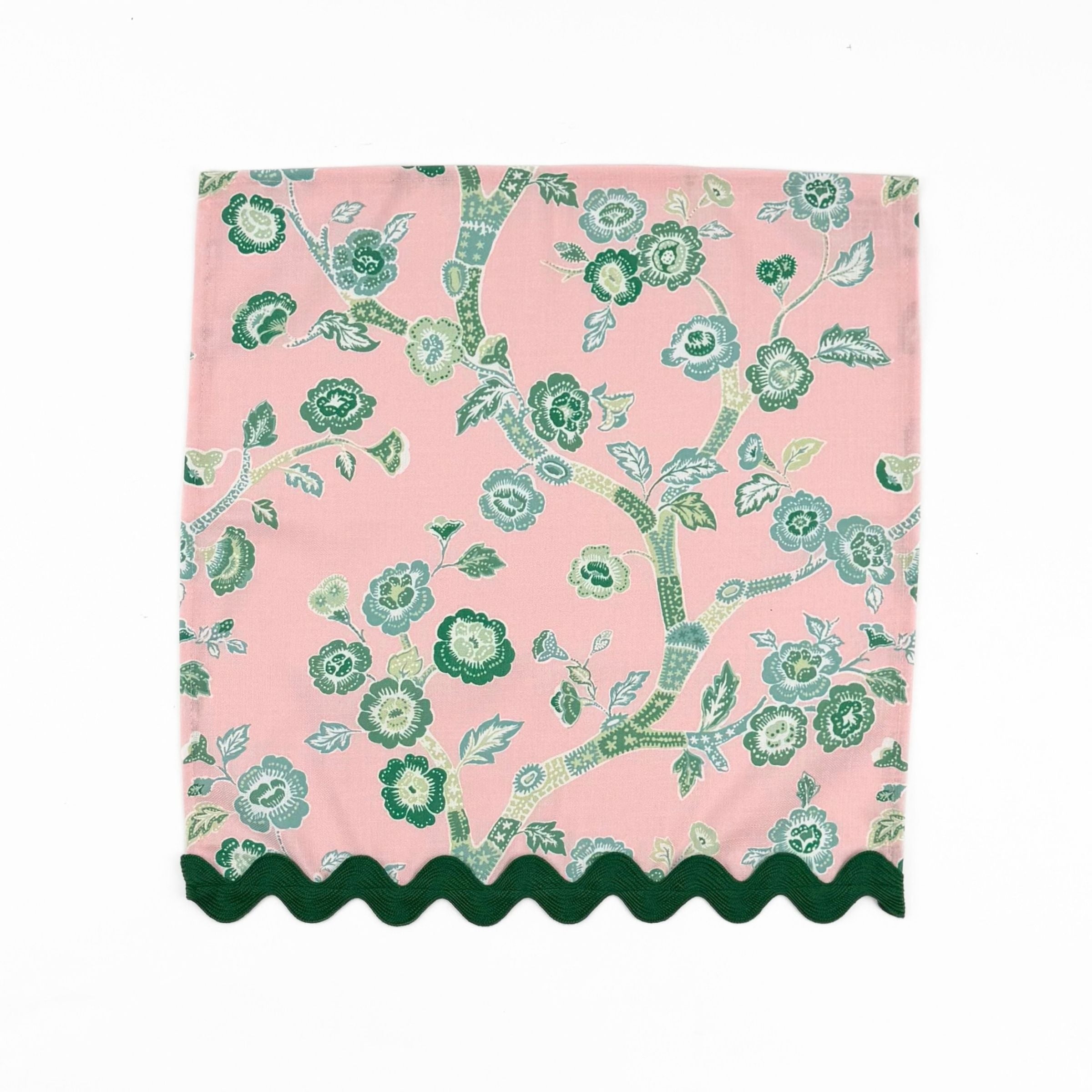 Pink cloth dinner napkins featuring elegant green chinoiserie florals, delicate branches, and dark green trim.