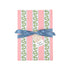 Front view of a present wrapped in pink and green Christmas wrapping paper with red ribbon and a paper tag