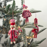 Three Christmas felt nutcracker ornaments in red, pink and white striped outfits on a christmas tree background