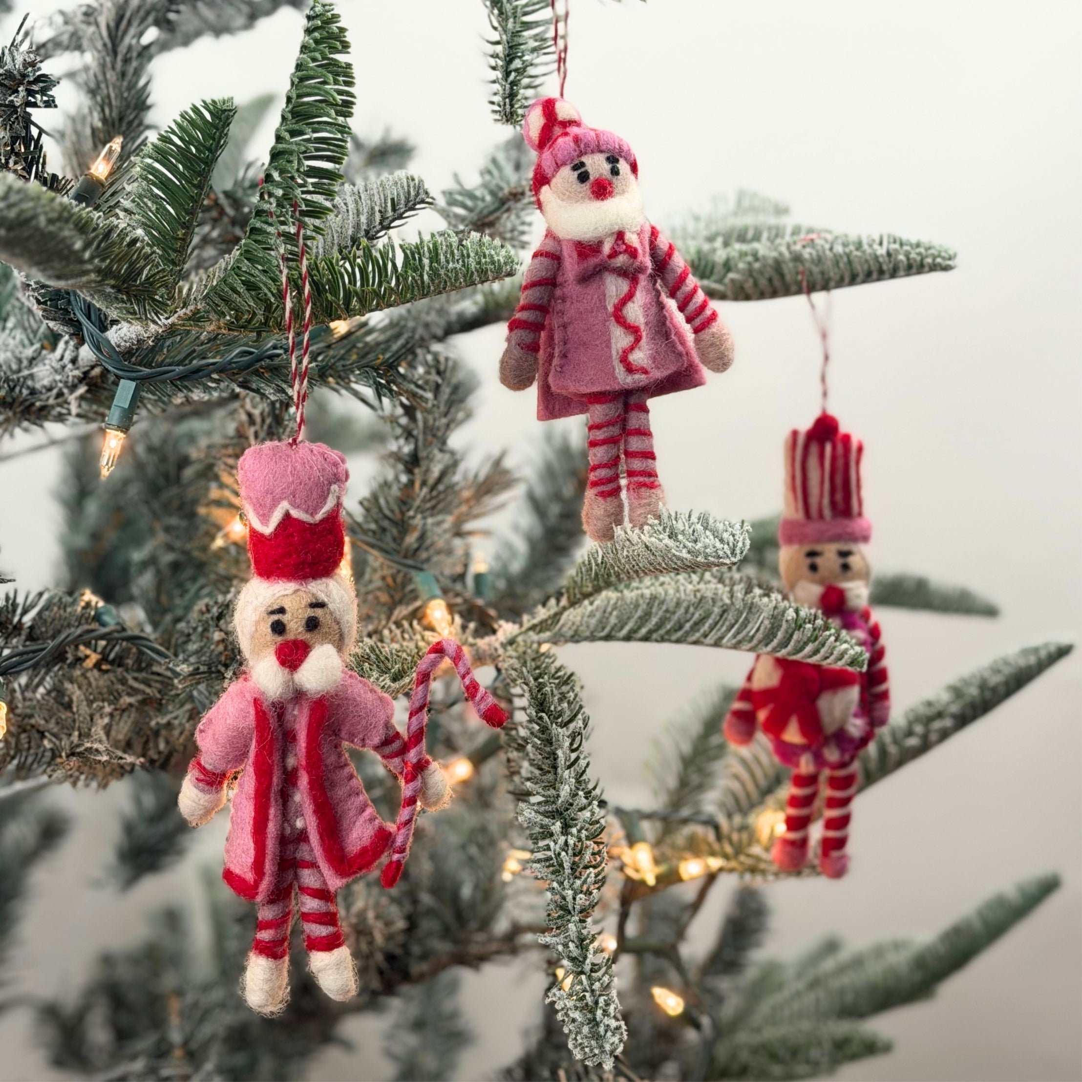 Three Christmas felt nutcracker ornaments in red, pink and white striped outfits on a christmas tree background