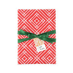 Red wrapping paper with a white geometric diamond pattern, wrapped around a gift box tied with a green ribbon and a small decorative tag