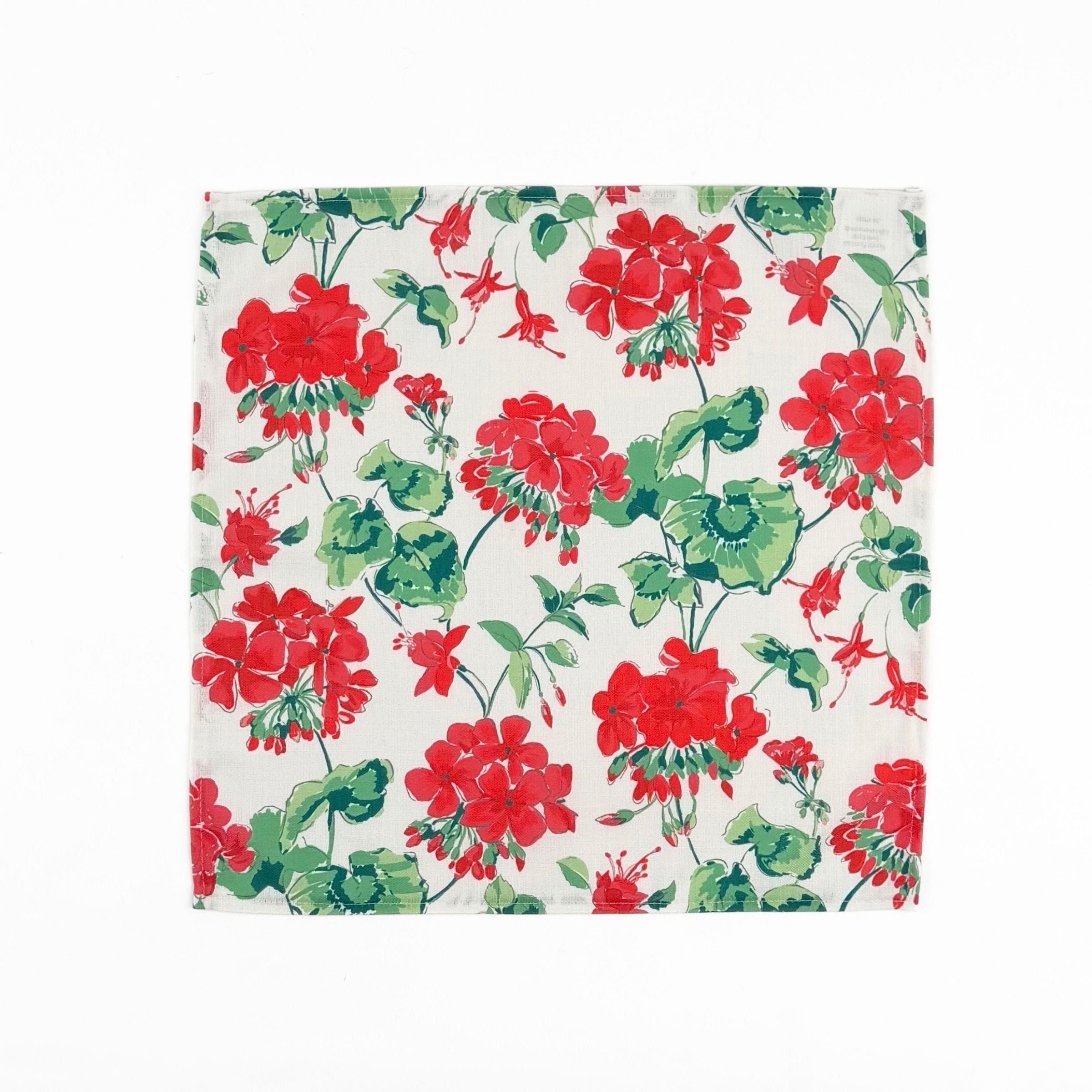 White cloth dinner napkins featuring vibrant red geranium flowers and lush green leaves for tablescapes.