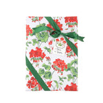a gift with a red geranium floral wrapping paper on a white background, tied with a green ribbon and a small paper tag.