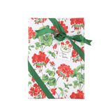 a gift with a red geranium floral wrapping paper on a white background, tied with a green ribbon and a small paper tag.