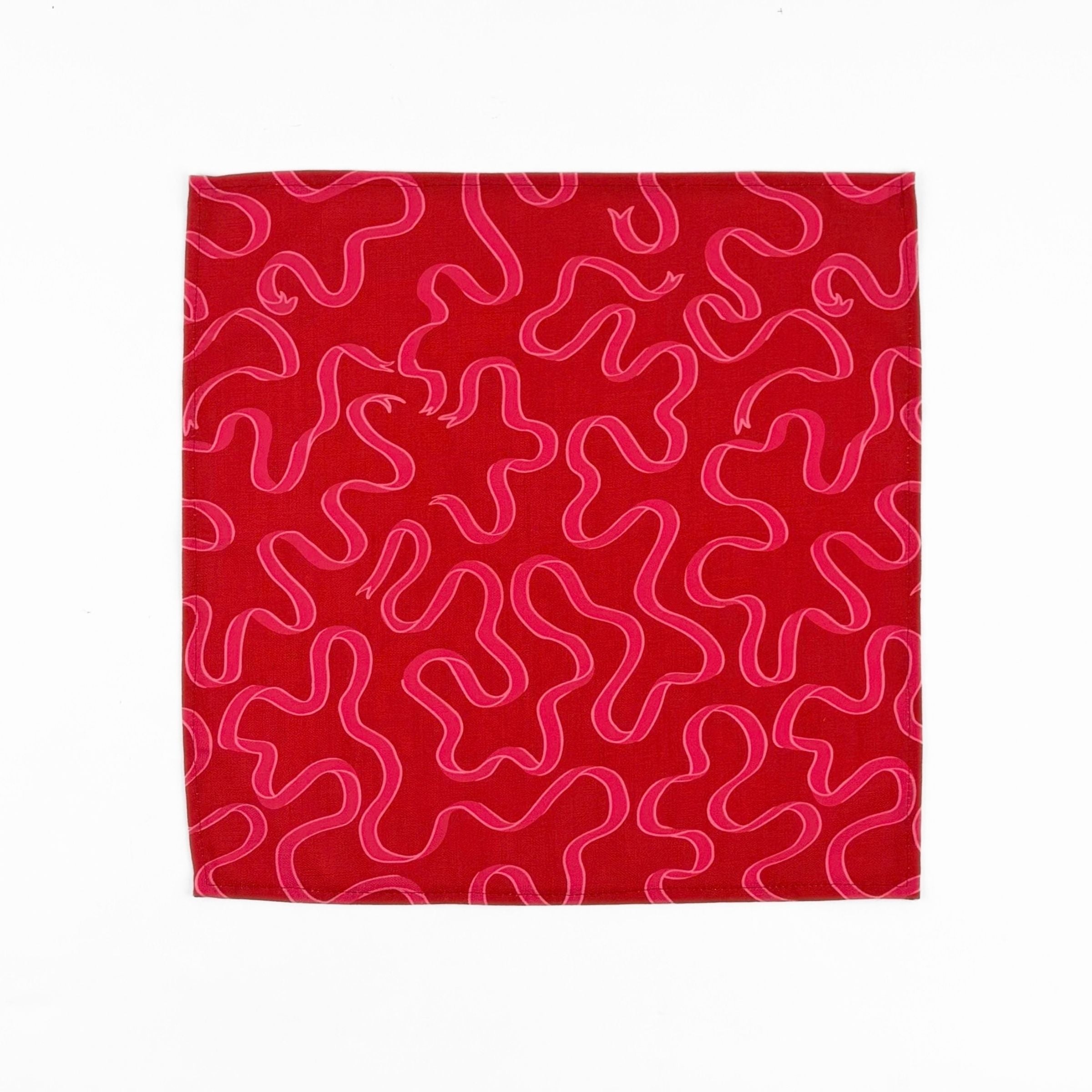 Red cloth dinner napkins featuring playful pink swirling ribbon patterns, perfect for festive table settings.