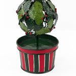 A close up of a tole metal three tiered holly topiary ball centerpiece with a striped red and green pot forming the base. 