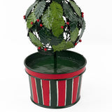 A close up of a tole metal three tiered holly topiary ball centerpiece with a striped red and green pot forming the base. 