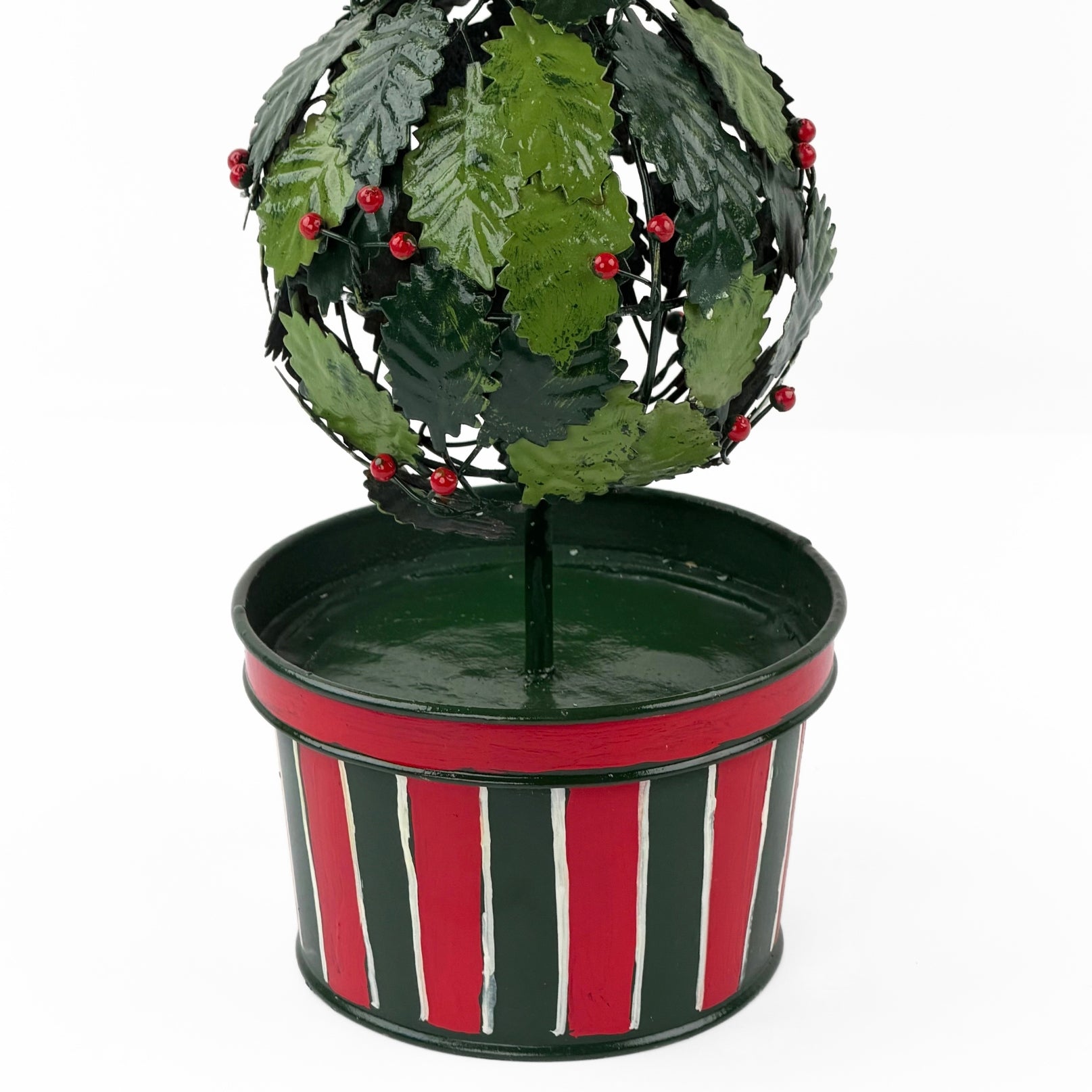 A close up of a tole metal three tiered holly topiary ball centerpiece with a striped red and green pot forming the base. 