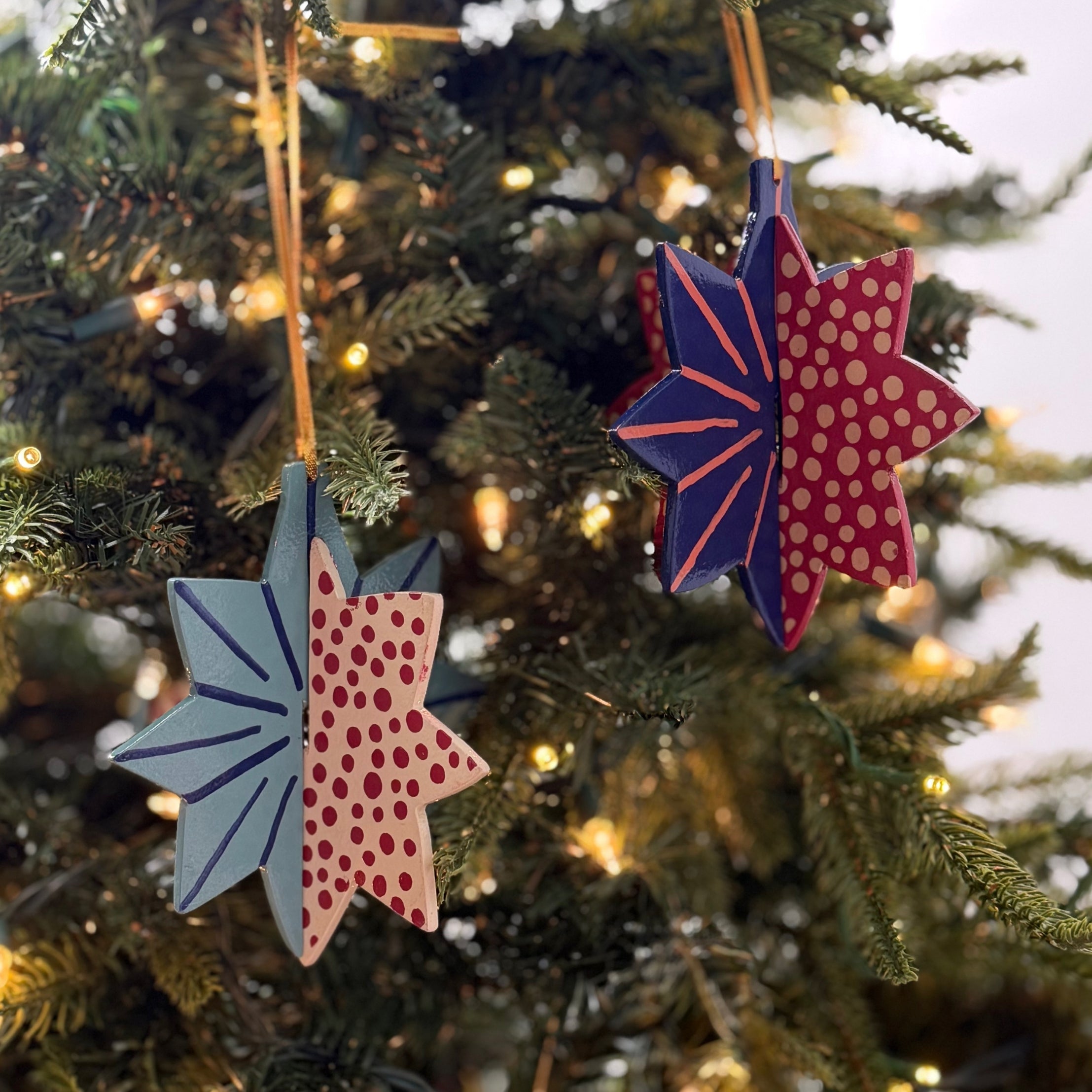 Hand-painted wooden patriotic star ornaments featuring red, white, and blue designs with decorative gold hanging cords.