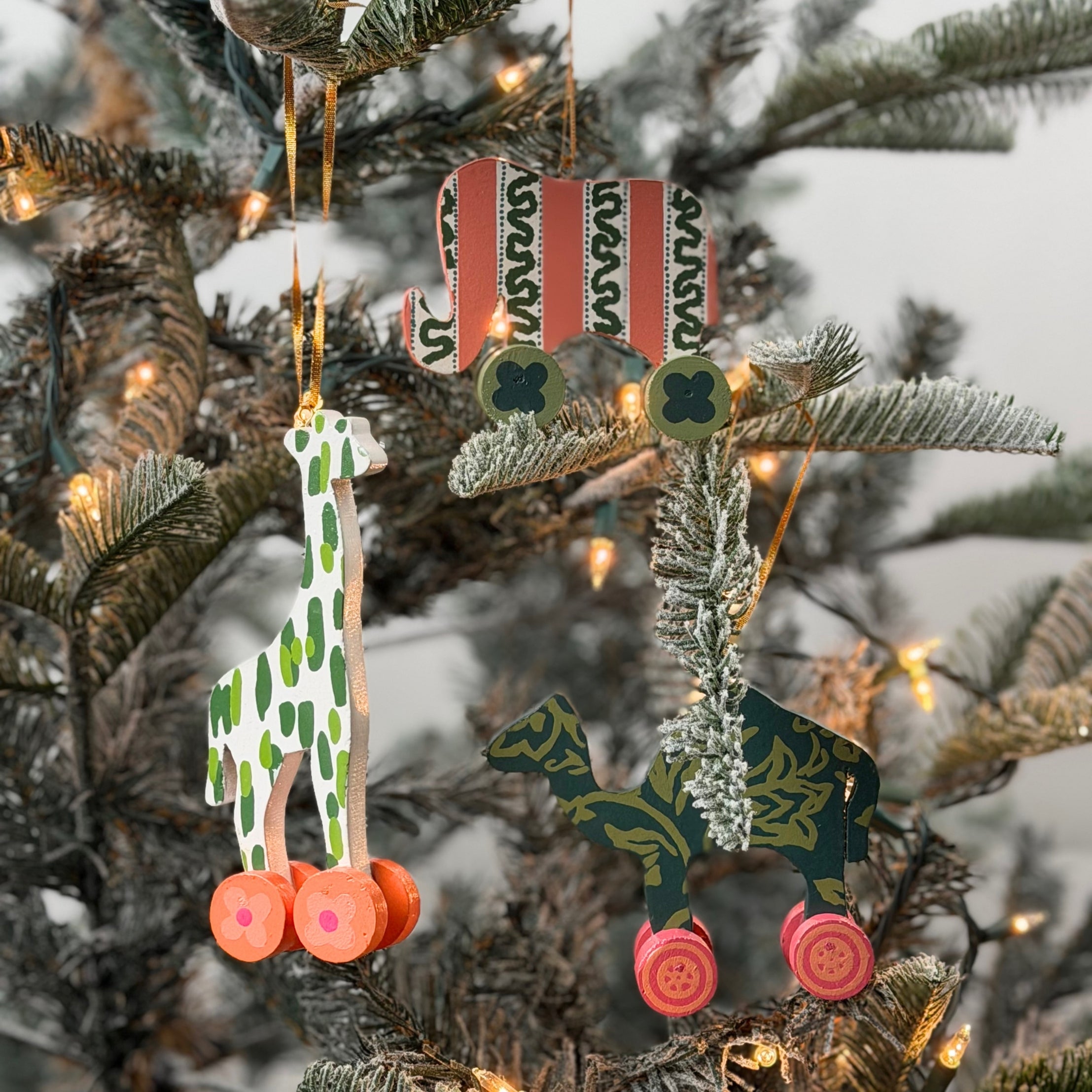 Wooden animal toy Christmas ornaments featuring colorful camel, elephant, and giraffe designs with decorative wheels.