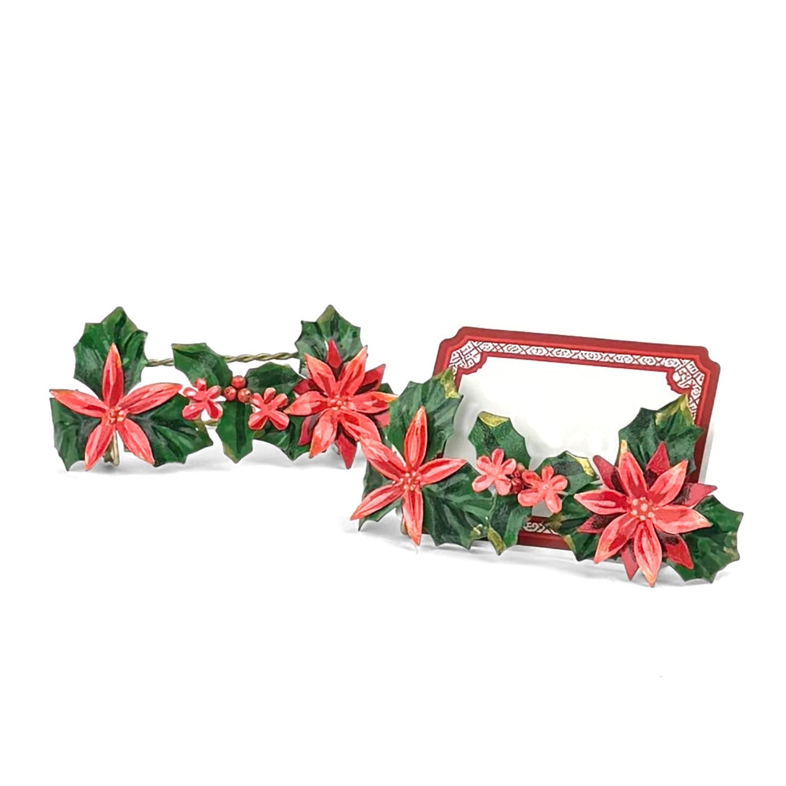 A pair of metal christmas place card holders decorated with red poinsettia flowers and holly leaves, with one containing a red bordered place card holder. 
