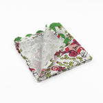 Folded White Christmas dinner napkins featuring festive mice, holly leaves, colorful gifts, and green scalloped trim.