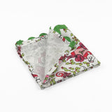 Folded White Christmas dinner napkins featuring festive mice, holly leaves, colorful gifts, and green scalloped trim.