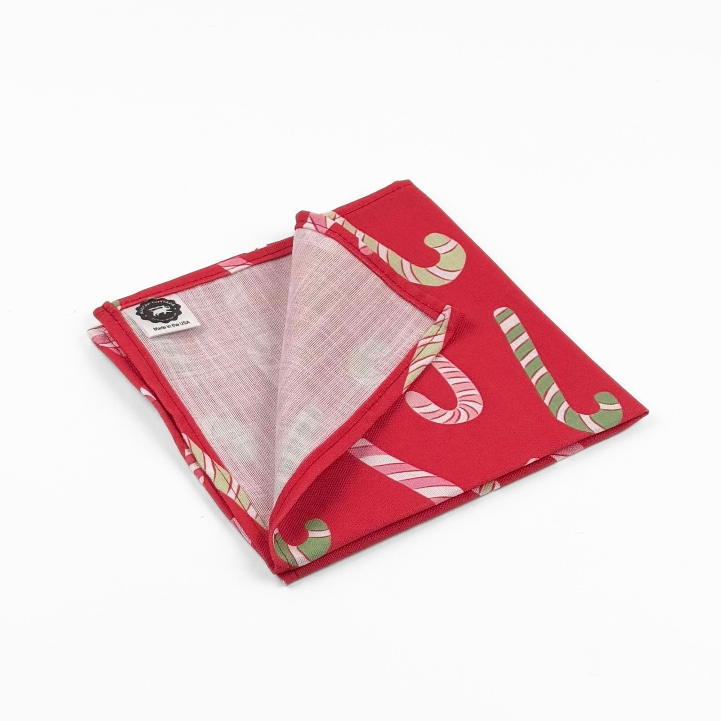 Folded Red cloth dinner napkins featuring playful pink, white, and green candy cane patterns for Christmas tablescapes.