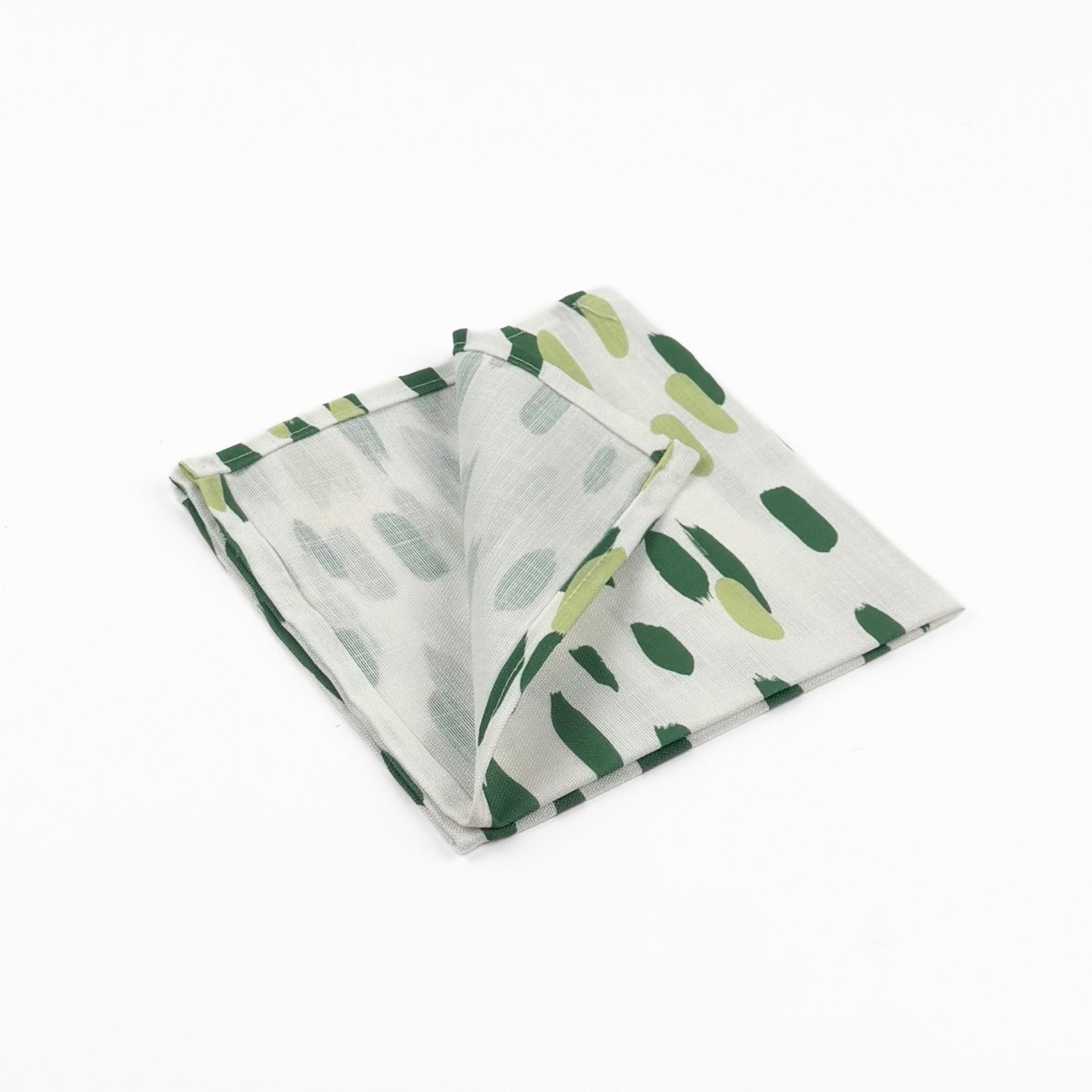 Folded White cloth dinner napkins featuring abstract green brushstroke patterns in varying shades for stylish tablescapes.