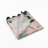 Folded Pink cloth dinner napkins featuring elegant green chinoiserie florals, delicate branches, and dark green trim.