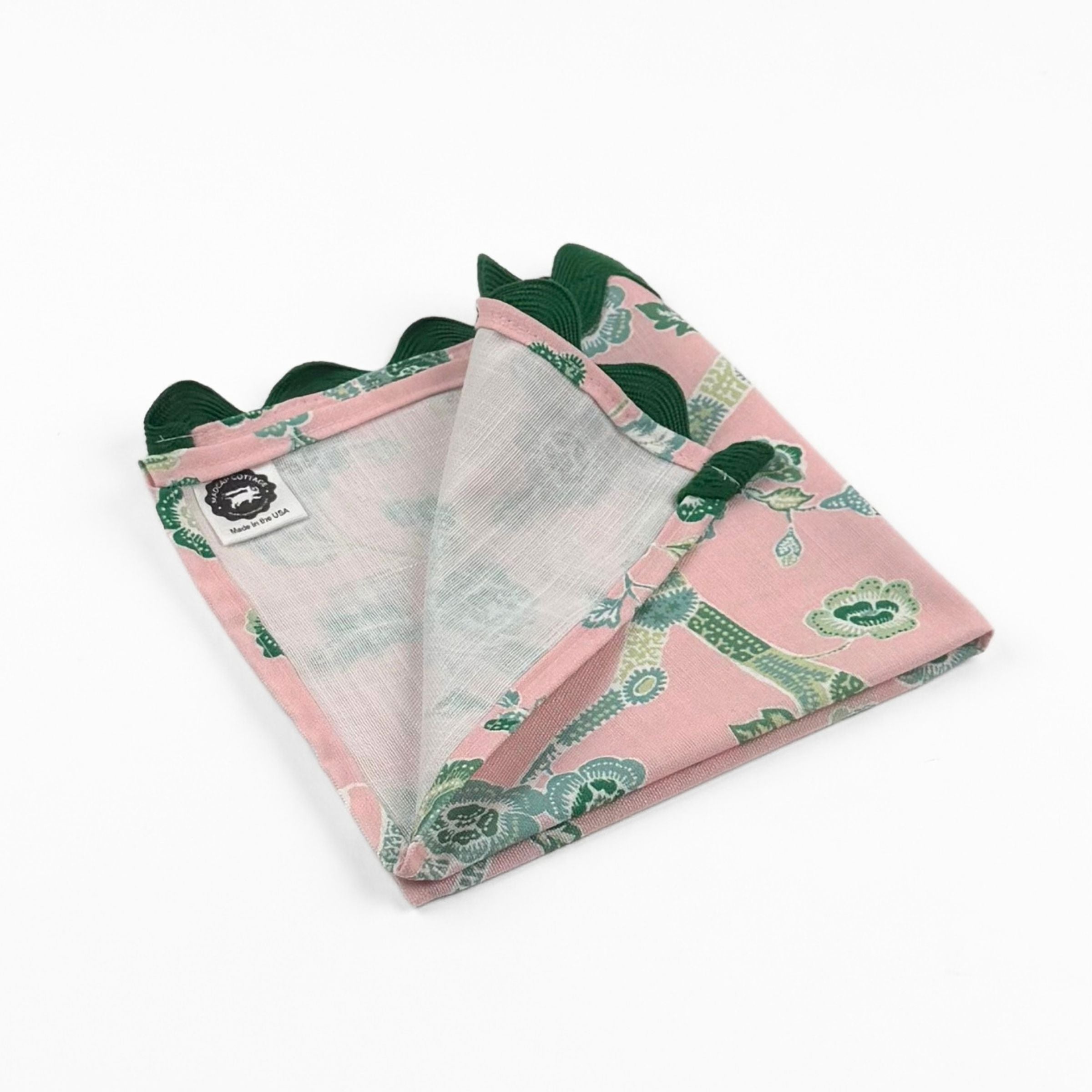 Folded Pink cloth dinner napkins featuring elegant green chinoiserie florals, delicate branches, and dark green trim.