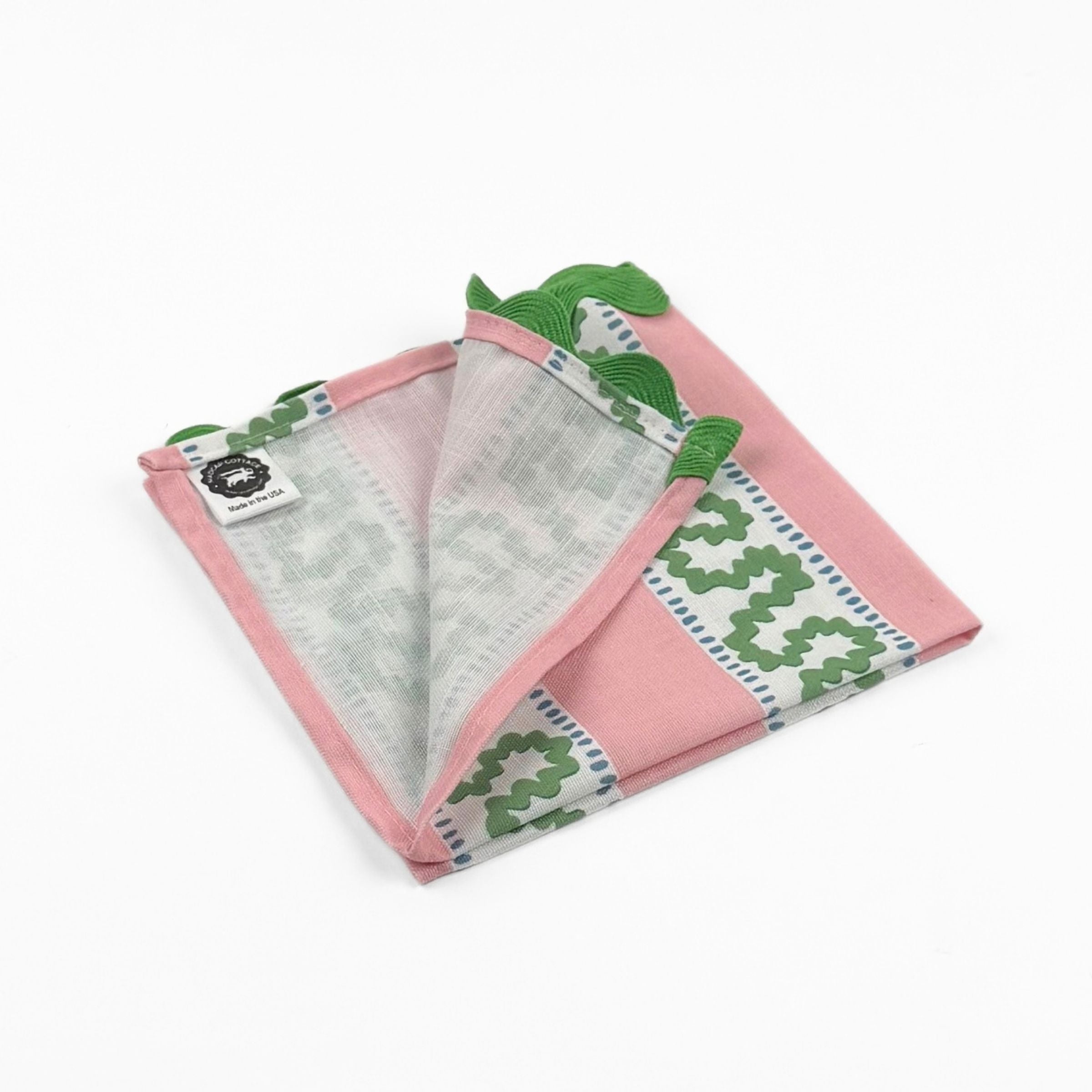 Folded Pink cloth dinner napkins featuring green wavy stripes, blue dotted accents, and green scalloped trim.