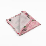 Folded Pink Christmas dinner napkins featuring swirling ribbons, nutcrackers, ballerinas, festive gifts, and whimsical holiday illustrations.
