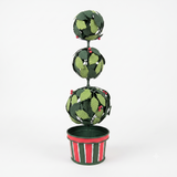 A decorative metal topiary tree with three stacked spherical tiers, covered in green leaf-shaped cutouts and small red berry accents, set in a striped red, green, and white pot against a plain white background.