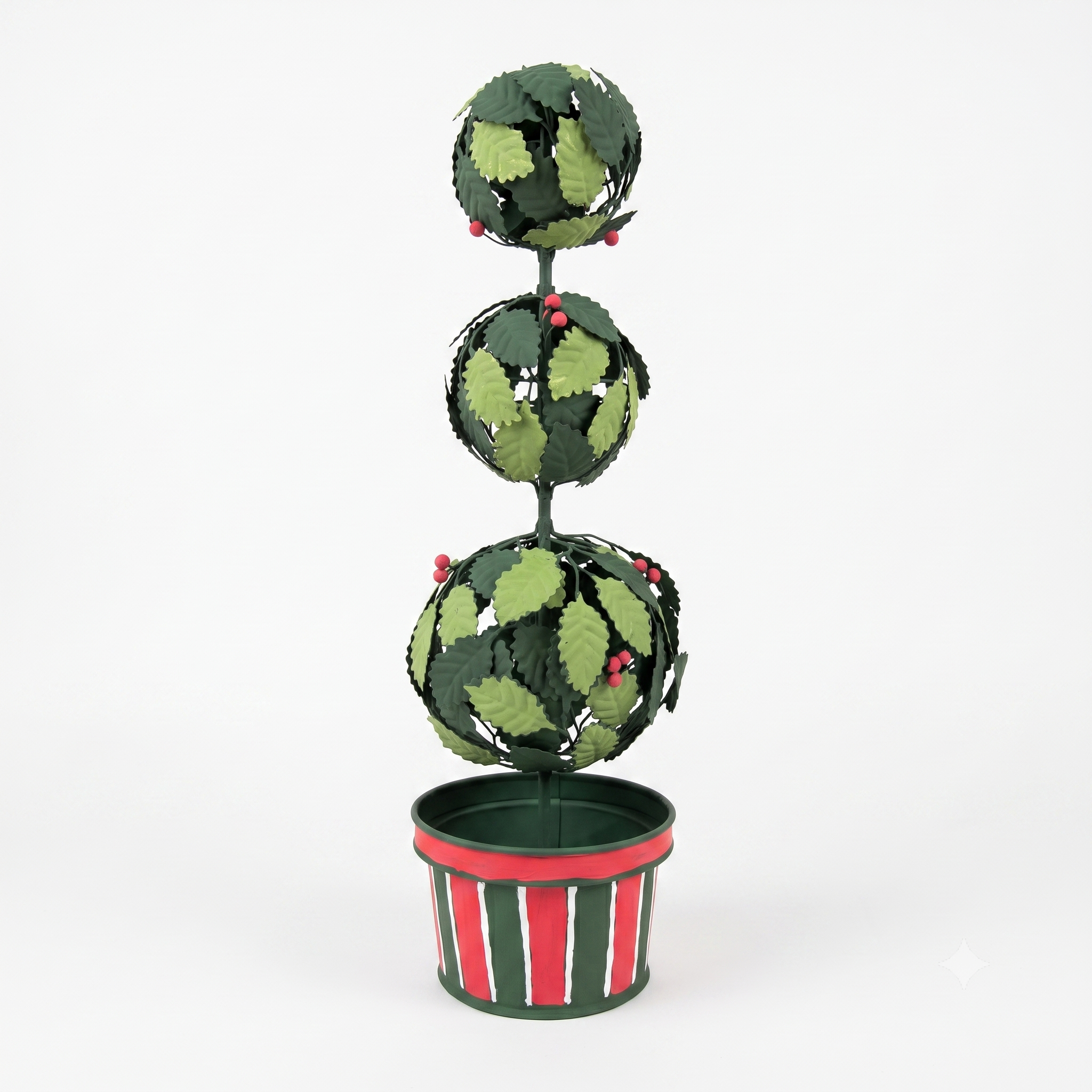 A decorative metal topiary tree with three stacked spherical tiers, covered in green leaf-shaped cutouts and small red berry accents, set in a striped red, green, and white pot against a plain white background.