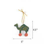 Wooden camel Christmas ornament featuring green floral patterns and pink wheels, measuring 4.5" by 5"