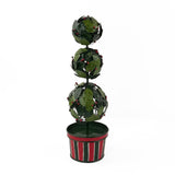 A tole metal three tiered holly topiary ball centerpiece with a striped red and green pot forming the base. 
