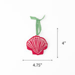Felt pink scallop shell Christmas ornament featuring white stripes, measuring 4" by 4.75"