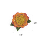 Orange felt flower ornament featuring yellow petals, green leaves, and gold sequins, measuring 6.5" by 5.5"