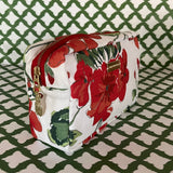 Front 3/4 view of Cottage Grove Geranium is a floral toiletries bag with a red, green, and white color scheme, featuring a geranium design.