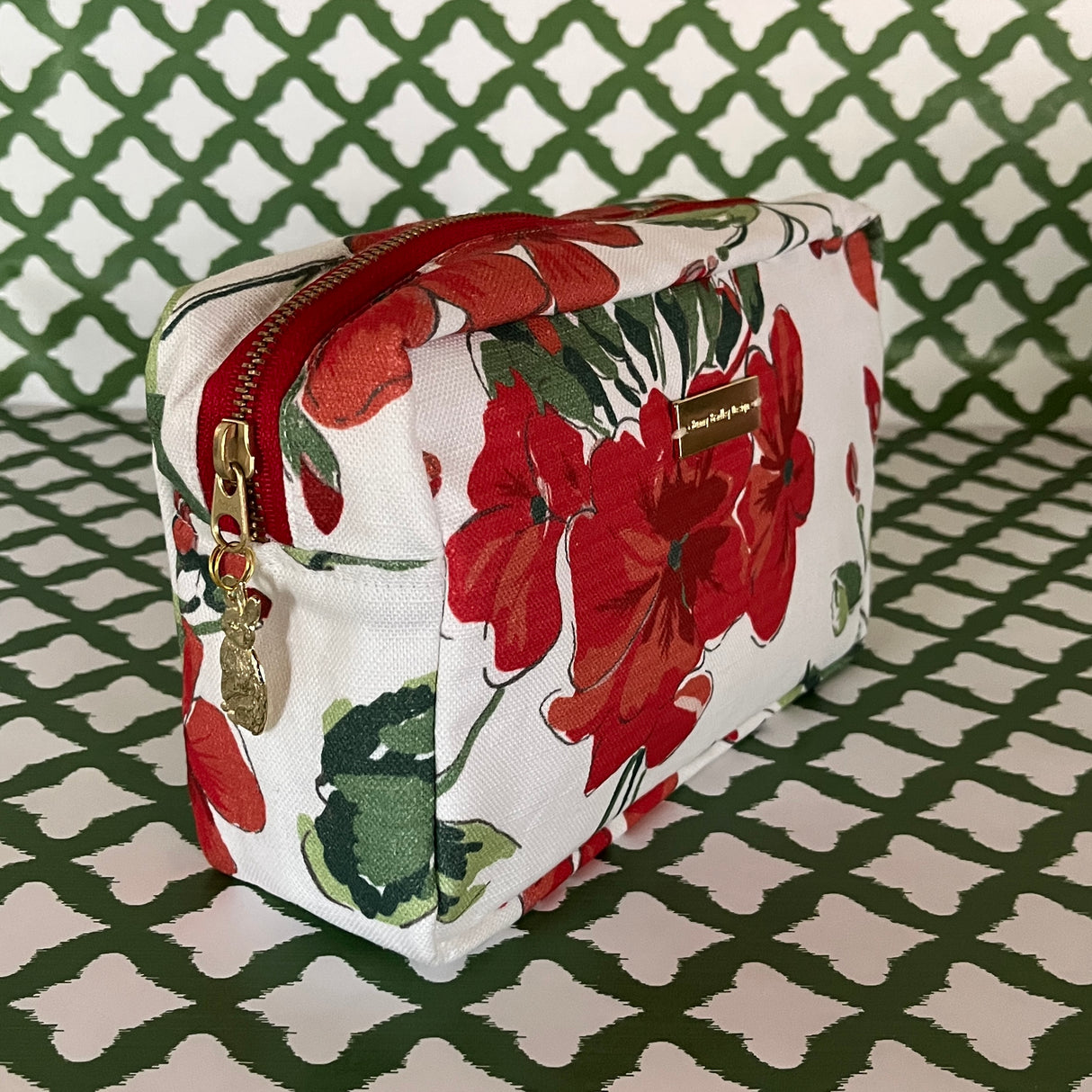 Front 3/4 view of Cottage Grove Geranium is a floral toiletries bag with a red, green, and white color scheme, featuring a geranium design.