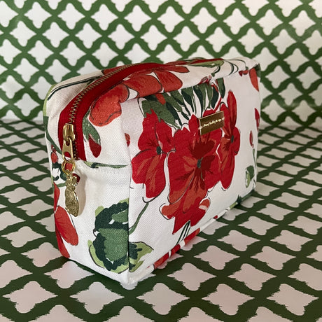 Front 3/4 view of Cottage Grove Geranium is a floral toiletries bag with a red, green, and white color scheme, featuring a geranium design.