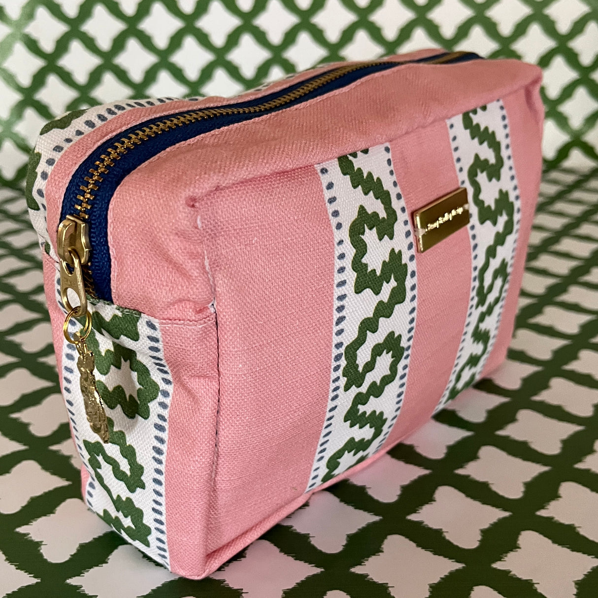 Front 3/4 view of Harbor Trail toiletry bag in Bahama pink with a green ribbon and blue dash motif.