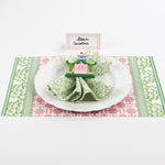 Christmas table setup featuring Bamboo Trellis Paper Place Card in candy pink, green patterned napkin, and white plate on festive pink and green holiday placemat.