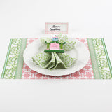 Christmas table setup featuring Bamboo Trellis Paper Place Card in candy pink, green patterned napkin, and white plate on festive pink and green holiday placemat.