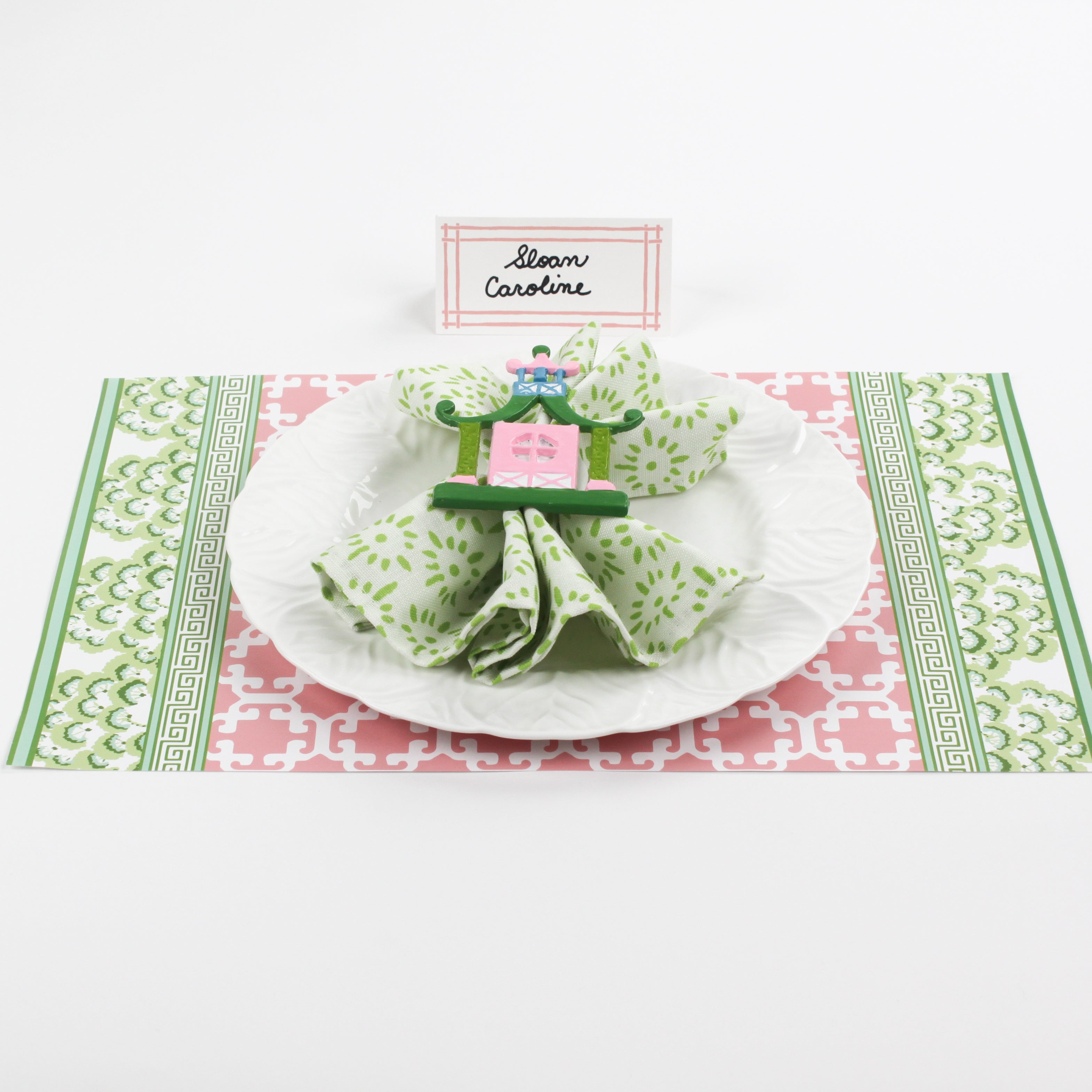 Christmas table setup featuring Bamboo Trellis Paper Place Card in candy pink, green patterned napkin, and white plate on festive pink and green holiday placemat.