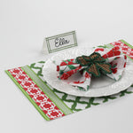 Side view of Bamboo Trellis Paper Place Card in forest green displayed on festive red and green Christmas placemat with floral napkin and rattan bow napkin ring.