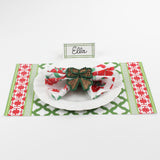 Christmas table setting featuring Bamboo Trellis Paper Place Card in forest green, white plate with floral napkin and woven bow napkin ring on red and green patterned placemat.
