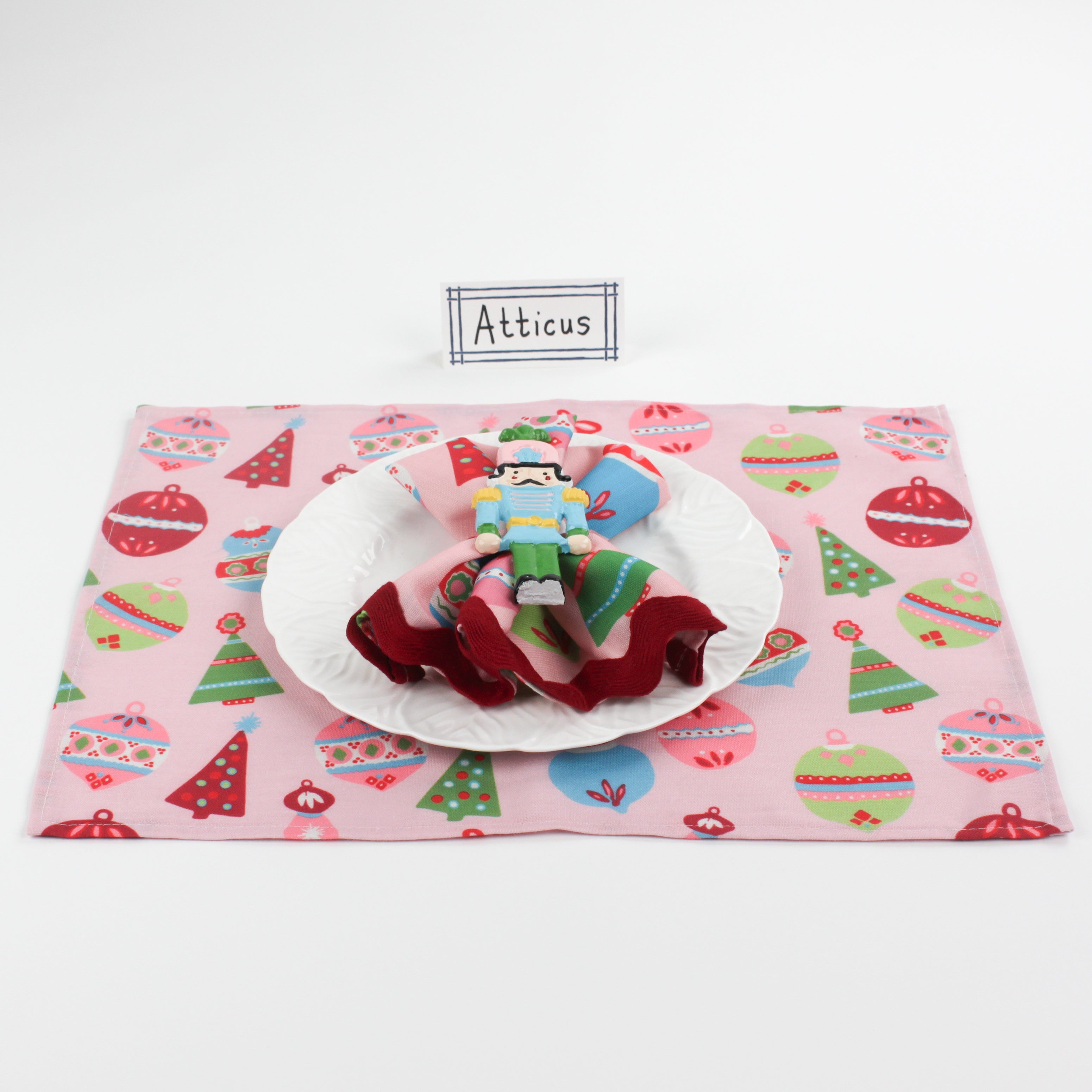 Christmas table setup featuring Bamboo Trellis Paper Place Card in navy blue, white plate, nutcracker napkin ring, and pink placemat with festive ornaments and trees.