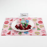 Christmas table setup featuring Bamboo Trellis Paper Place Card in pool blue, white plate, nutcracker napkin, and pink holiday placemat with ornaments and trees.