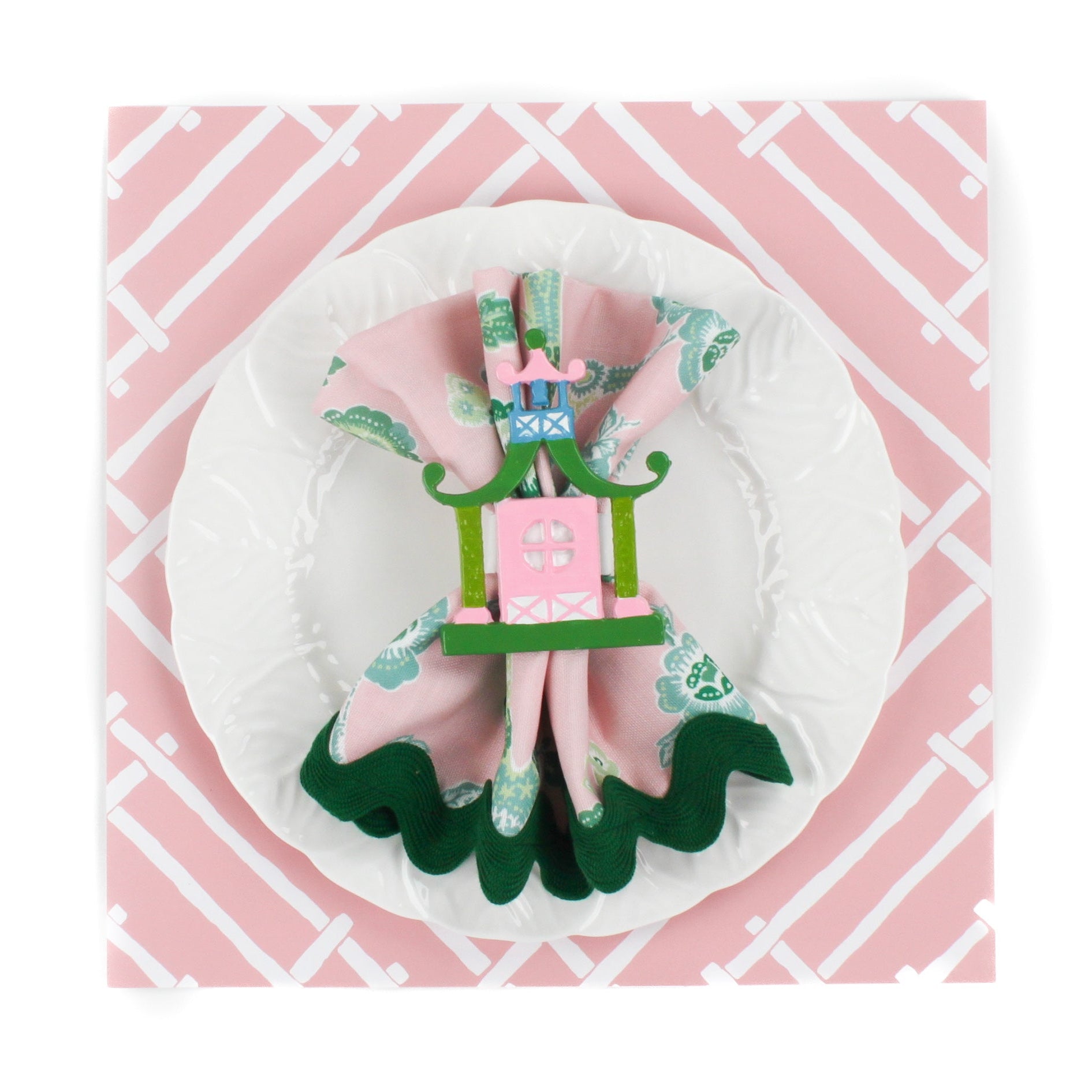 pink paper placemats with a white bamboo design called Island house by Madcap Cottage. A white plate is placed on top of it with a cloth and a pagoda napkin ring