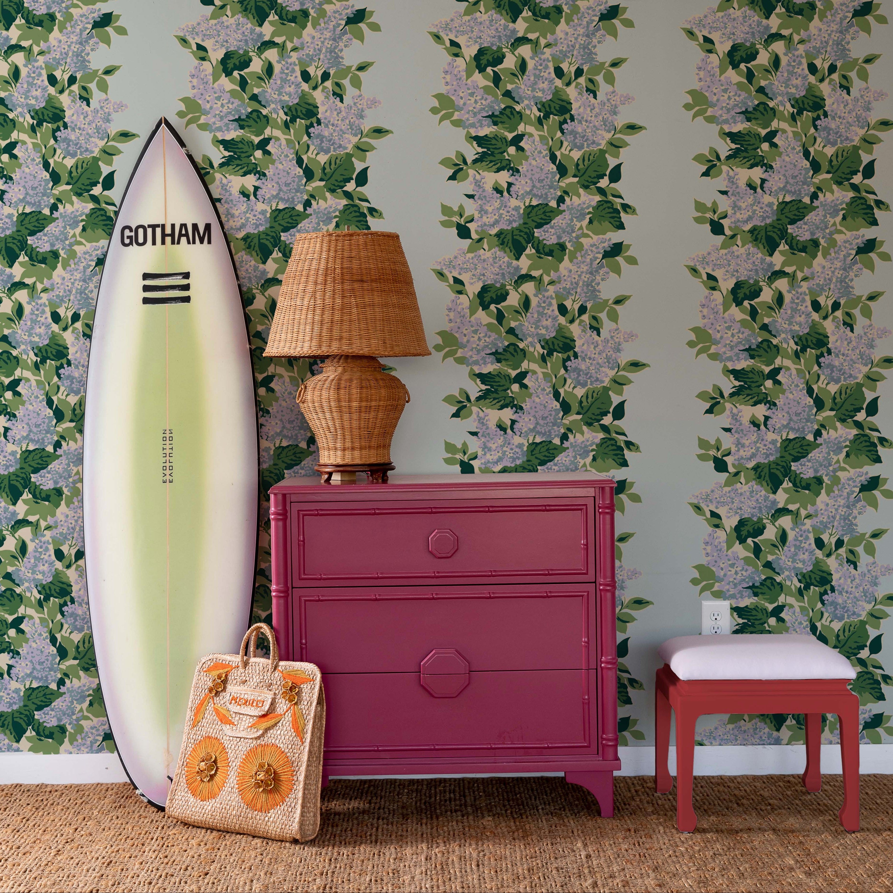 a room scene with a blue floral hydrangea wallpaper with a surfboard and a lamp, and red chest of drawers in the foreground.