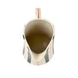 Blue and red striped pitcher top view with cream ceramic interior and curved spout opening.