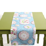 Blue table runner with decorative floral plate motifs displayed on a green table.