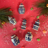 A set of six blue and white miniature ceramic ginger jars with Christmas ornaments, displayed against a red background with green pine branches and holiday decorations.