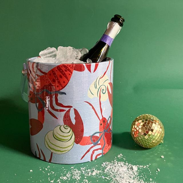 Blue ice bucket filled with ice and champagne features a green shell and red lobster print