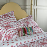 Bed with red and white bow patterned bedding and a colorful pillow.
